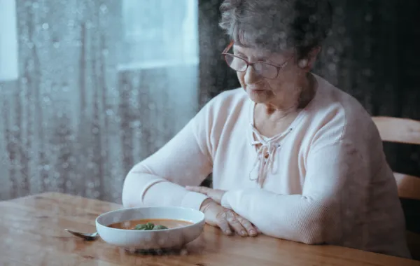 Foto de una mujer mayor sentada ante un plato de comida con cara de preocupación