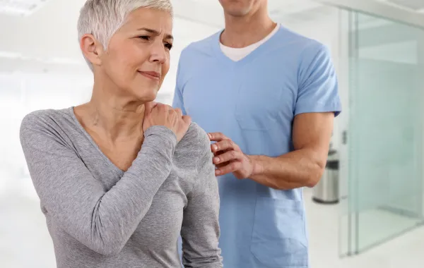 Foto de una mujer adulta con cara de dolor mientras se toca un hombre y está acompañada de un médico