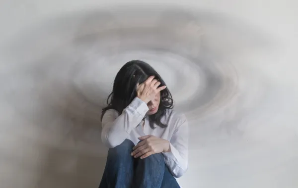 Foto de una mujer joven sentada en el suelo y con la mano apoyada en la cabeza con gesto de dolor