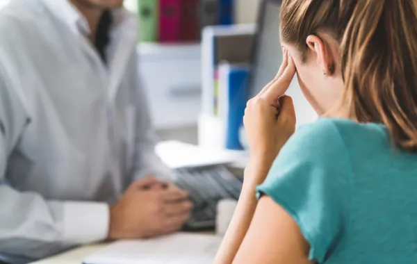 Foto de una mujer con las manos en la cabeza y en una consulta con el medico