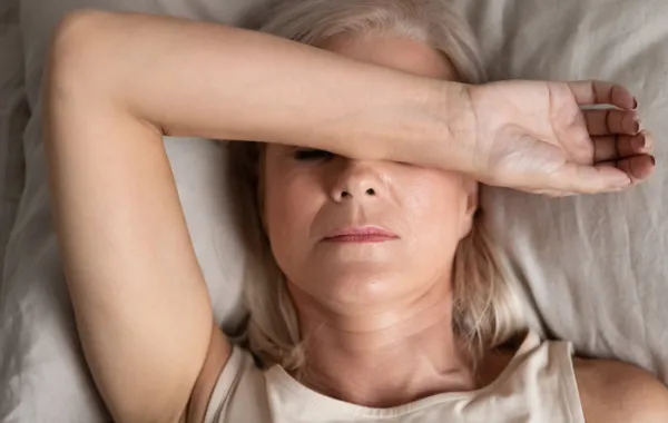 Foto de una mujer adulta tumbada y que se tapa con el brazo los ojos y parte de la cara