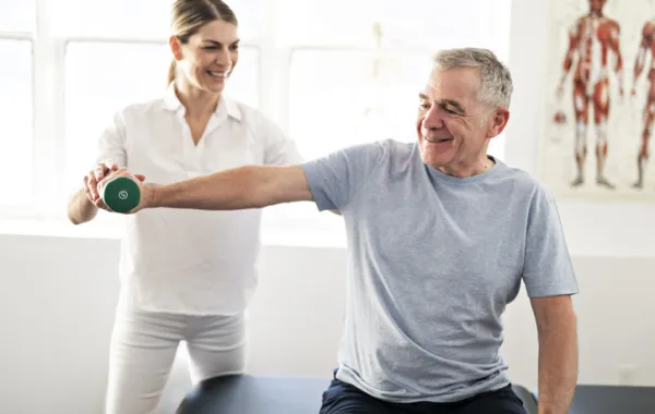 Foto de un señor adulto realizando ejercicios con el brazo con una fisioterapeuta