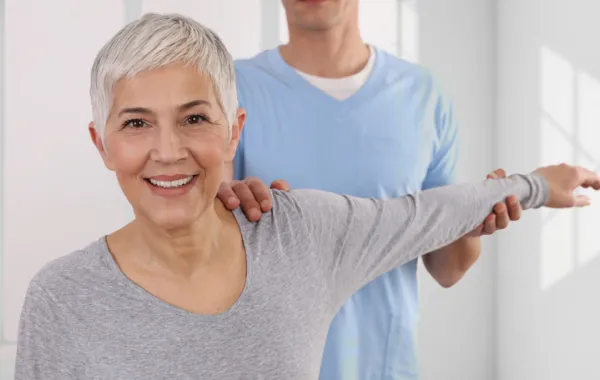 Foto de una mujer adulta haciendo ejercicio con un brazo atendida por un fisioterapeuta
