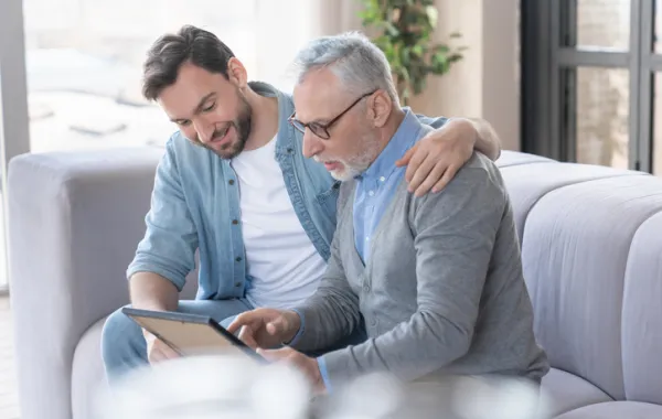Foto de un señor mayor acompañado por otro hombre joven mientras leen juntos