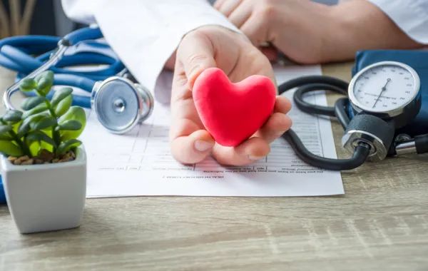 Foto de la mano de un médico que sostiene un corazón de goma y rodeado de aparatos médicos