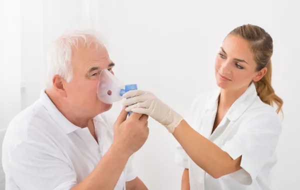 Foto de un señor mayor que respira con un aparato de oxigeno ayudado por una enfermera