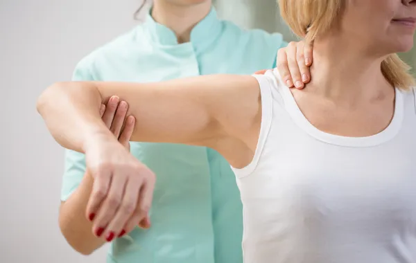 Foto de una mujer adulta que realiza ejercicios con el brazo ayudada por una fisioterapeuta