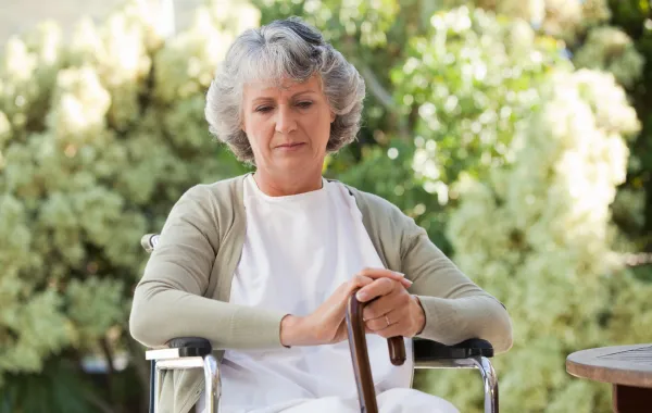 Foto de una mujer mayor sentada en una silla de ruedas y con un bastón en la mano