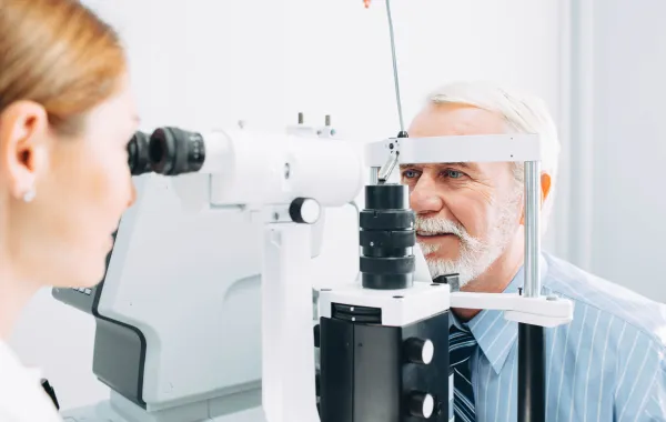 Foto de un señor mayor que es revisado de la vista por un óptico optometrista