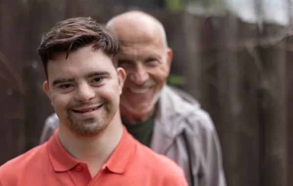 Foto de un joven con sindrome de down acompañado por un señor mayor y sonriendo los dos