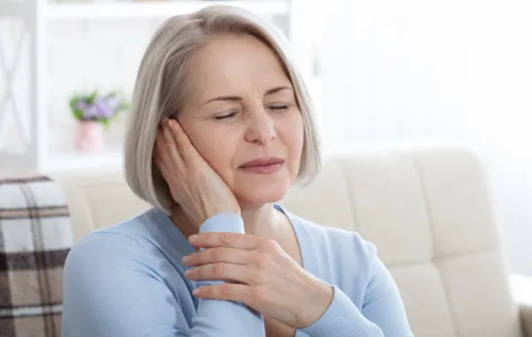 Foto de una mujer con la mano puesta en la oreja y con cara de dolor