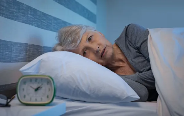 Foto de una mujer mayor tumbada en la cama con los ojos abierto y mirando el despertador
