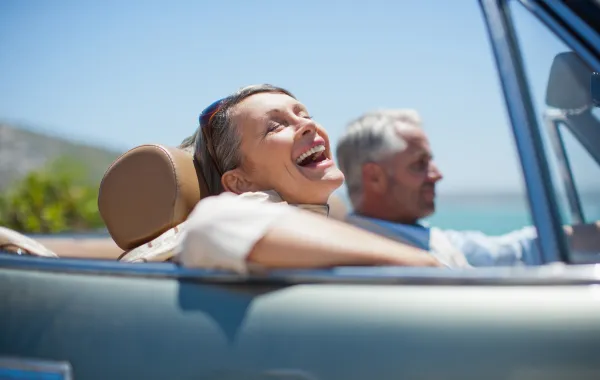Foto de una pareja de personas maduras que sonrien mientras van en un coche descapotable