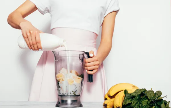Foto de una persona que vierte leche de una botella en una licuadora