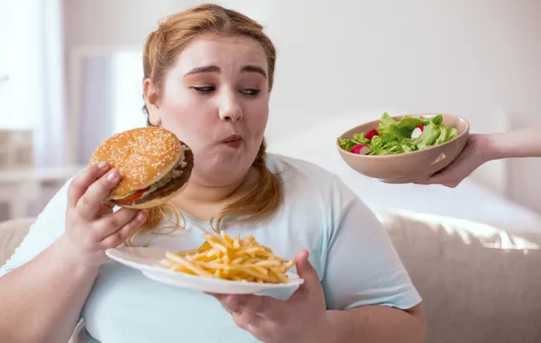 Foto de una chica joven con sobrepeso comiendo comida no saludable