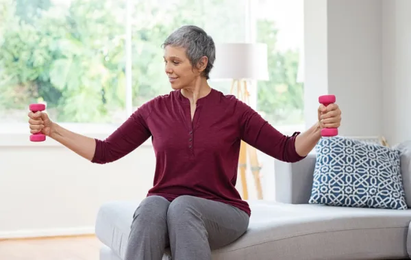 Foto de un mujer adulta haciendo deporte con dos pesas en las manos en su casa
