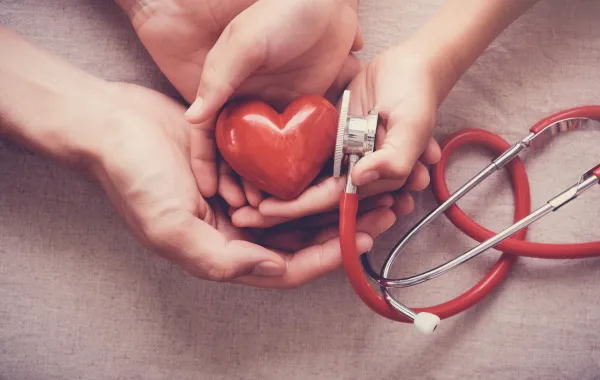 Foto de unas manos que sujetan una figura con forma de corazón al lado de un fonendo