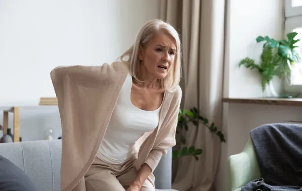 Foto de una mujer adulta con la mano en la espalda y gesto de dolor