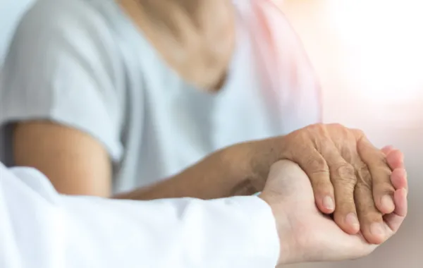 Foto de una mano de persona mayor sostenida por otra mano de un médico