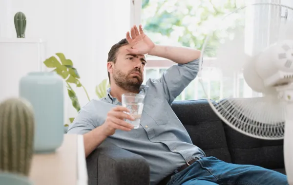 Foto de un señor sentado en un sillón con sintomas de sofoco por calor y un vaso de agua en la mano