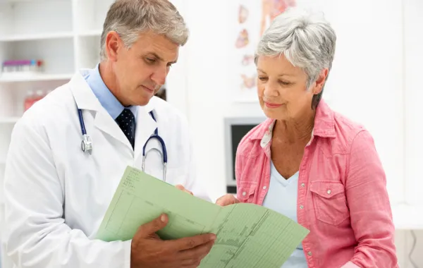 Foto de una mujer mayor acompañada de un médico que le muestra unos documentos