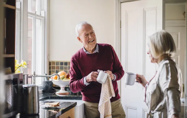 Foto de dos personas mayores charlando en una cocina mientras limpian los platos