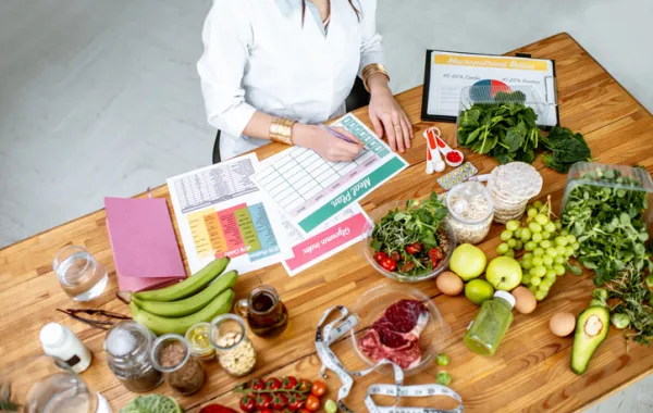 Foto desde arriba de una mesa con comida sana variada y una cocinera preparandola