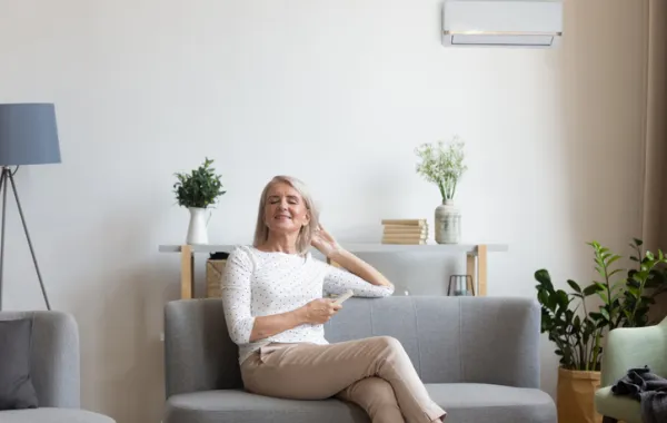 Foto de una mujer sentadadebajo de un sofá con un aparato de aire acondicionado encima