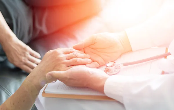 Foto de una manos de persona mayor que son cogidas por otras manos de un médico