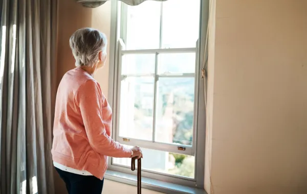 Foto de una mujer mayor mirando fuera de la ventana de su casa