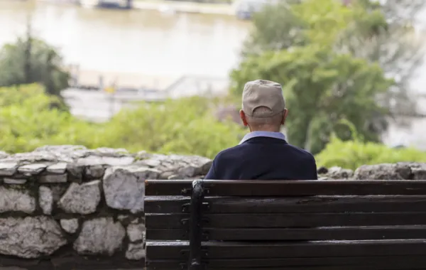 Foto de espaldas de un señor mayor sentado en un banco en un jardin