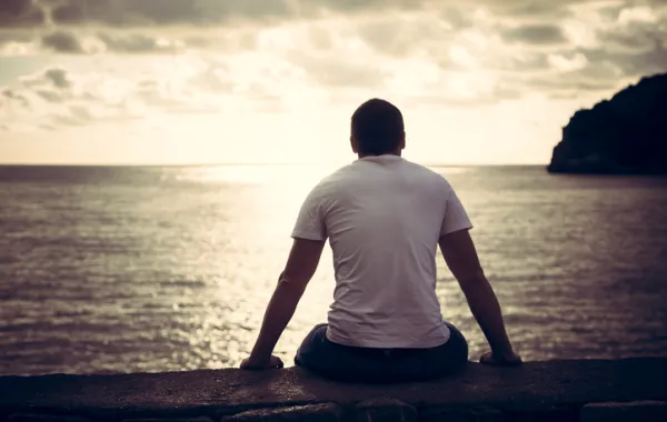 Foto de una persona sentada de espaldas mirando un atardecer