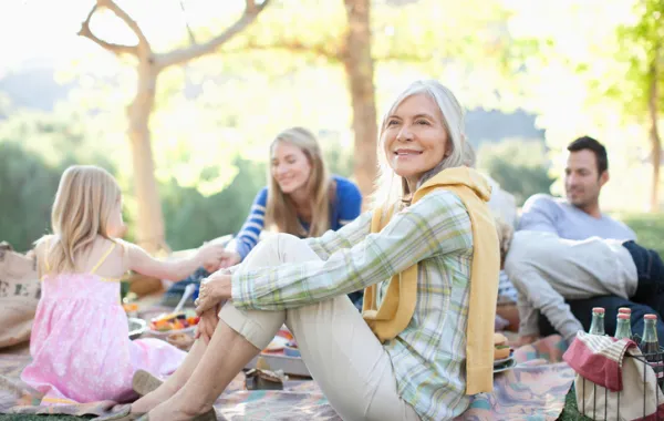 Foto de una señora adulta sonriendo y sentada en un jardin rodeada de gente más joven
