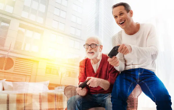 Foto de un señor mayor y un señor joven jugando con unos mando de una consola
