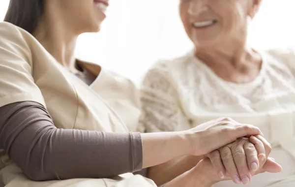 Foto de una mujer mayor acompañada de una enfermera que le sostiene la mano