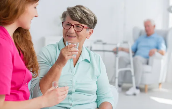 Foto de una mujer mayor que bebe agua de un vaso ofrecido por una mujer joven