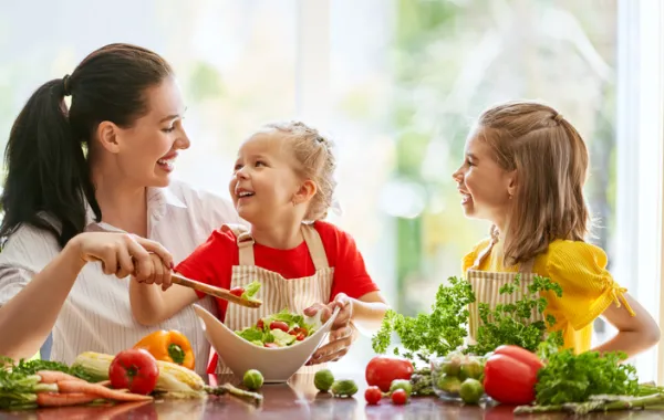 Foto de una madre con sus hijos comiendo ensalada y fruta