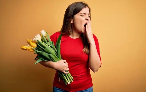 Foto de una mujer que sostiene unas flores mientras bosteza por cansancio