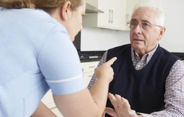 Foto de un señor mayor con cara seria mientras que una enfermera le increpa con el dedo
