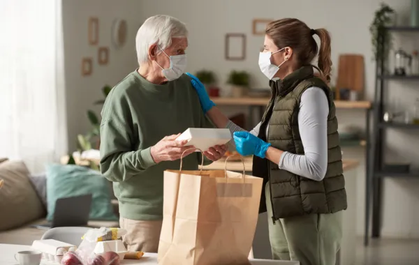 Foto de un señor mayor recibiendo una bolsa con comida de una asistente social