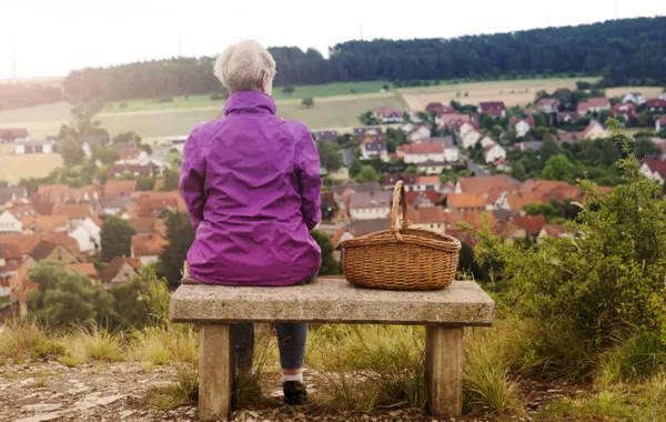 Foto de una señora mayor sentada en un banco mirando el campo