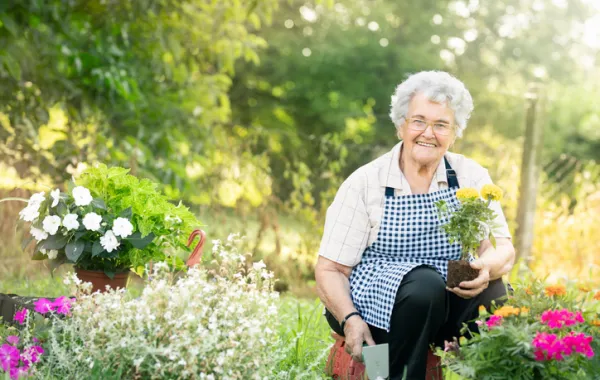 Foto de una mujer mayor en un jardín y colocando macetas de flores