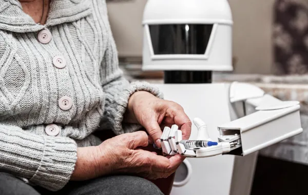 Foto de las manos de una persona mayor cogiendo un bolígrafo de una mano de un robot