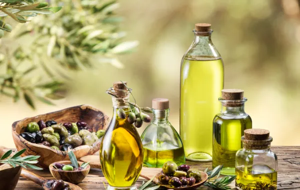 Foto con varios tipos de botellas de cristal con aceite de oliva rodeados de varios tipos de aceituna