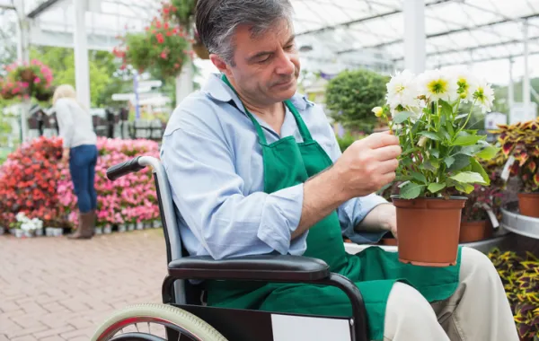 Foto hombre en silla de ruedas arreglando una maceta con un planta