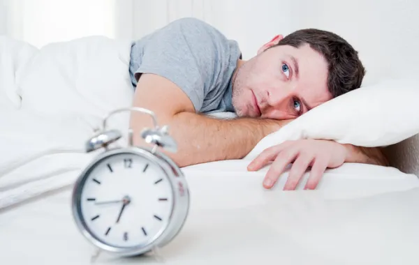 Foto hombre tumbado en una cama con los ojos abiertos y un despertador