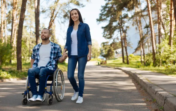 Foto de un joven en silla de ruedas acompañado por una mujer joven mientras pasean