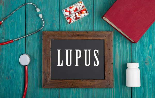 Foto de un cartel que pone lupus rodeado de unas pastillas y material medico