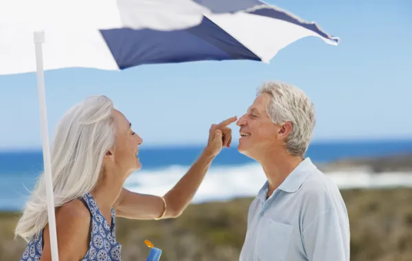 Foto de una pareja madura debajo de una sombrilla y echándose crema solar en la cara