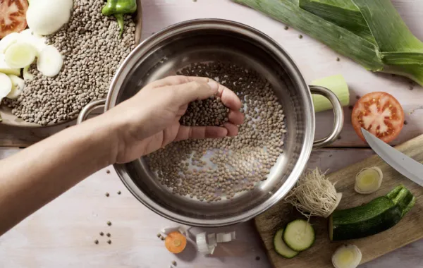 Foto de una mano que prepara en la cazuel un guiso con legumbres y verduras
